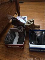 Photo showing two pairs of brown women's boots with faux fur lining in their boxes on a wooden floor.