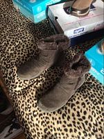 Photo showing a pair of ladies dark brown boots with plush faux-fur ankle cuff and side zipper next to shoe boxes