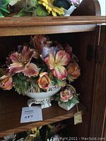 Wide view of the larger porcelain floral arrangement and smaller basket piece on wood shelf