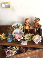 Wide shot showing entire lot on a wooden shelf including figurines, plates, flowers, and snow globes