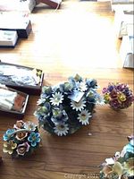 Overhead photo of three porcelain flower arrangements on wooden floor, showing colorful flowers and shapes.