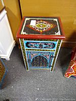 Full front view of the hand painted Moroccan wood table showing colorful geometric patterns, drawer and door.