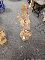 Solid driftwood sculpture standing upright on carpeted floor, showing natural wood texture and abstract form.