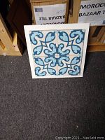 Close-up photo of four blue and white Moroccan cement mosaic tiles arranged in a white frame showing intricate floral and geometric patterns.