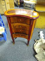 Full frontal view of curved wood jewelry chest with reddish legs and brass accents