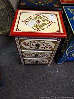 Front view of the side table showing the three drawers and top hand-painted design.