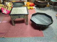 Set of three Moroccan tables on a carpeted surface, including two square tables with pierced metalwork and an octagonal carved wooden table.