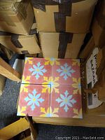 Four Moroccan cement mosaic tiles arranged on the floor, showing the floral geometric mosaic pattern in red, yellow, and turquoise colors.