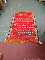 Full view of the red Moroccan Berber wool rug laying flat on the floor showing the full length and fringe end.
