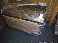 Closed Moroccan trunk with wood and decorative metal overlay, wrapped in plastic with visible decorative pattern on metal overlay.