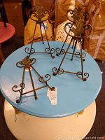 Four collapsible wrought iron picture holders arranged on a blue round table with visible decorative leaf and scroll motifs.