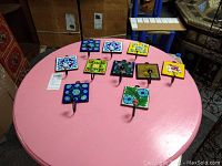 Photo showing the set of 10 hand painted ceramic tile coat hooks arranged on a pink surface, displaying various colorful floral and geometric designs.