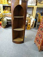 Moroccan wood three-shelf corner unit with arch-shaped top, dark wood finish, shown standing in a warehouse environment.
