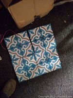 Four handmade Moroccan cement mosaic tiles arranged to display their repetitive symmetric pattern in blue, white, and beige colors.