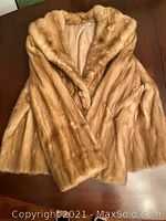Front angled view of blonde mink fur coat on wooden surface showing collar, sleeves, and partial front.