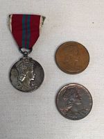 Photo showing the front side of the medal with ribbon, and two commemorative coins featuring Queen Elizabeth II's crowned profile.