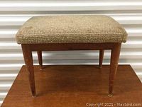 Front view of footrest showing teak legs and beige upholstered top