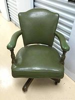 Front view of green leather office chair showing seat, backrest, wooden arm supports and caster-equipped swivel base.