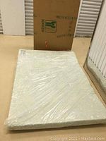 Mattress pad fully unwrapped and flat on floor, original packaging box in background