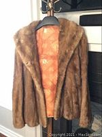 Front view of whiskey blonde mink coat hanging on black hanger, showing soft fur exterior and patterned textile lining.