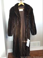 Full-length front view of coat on wooden hanger against wall showing overall length and fur texture