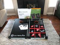 Full view of the two foldable Outbound game boards with beanbags and instruction manual on a carpet.