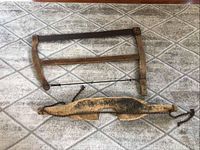 Antique wooden frame saw with metal blade and wooden shoulder yoke for carrying buckets, displayed on a patterned floor.