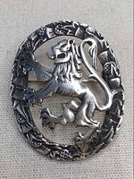 Front close-up of the silver pin depicting a detailed rampant lion within an oval border of thistle motifs on a fabric background.