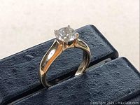 Ring angled on display vise showing yellow gold band and white gold head with round brilliant diamond