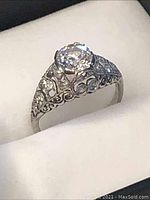 Front angle view of ring in box showing center diamond and filigree shoulders