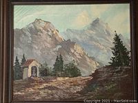 Framed oil painting showing mountainous landscape with chapel and trees.
