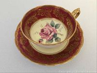 Angled front view of tea cup nested in saucer showing rose motif and gold gilt border