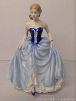 Front view of the Royal Doulton Susan figurine showing blue dress with white front details and light blue skirt, approx. 9 inches tall.