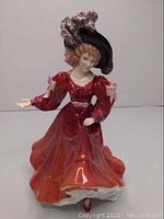 Front view of the Royal Doulton porcelain figure depicting a woman in red/orange gown and large hat.