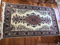 Full view of the rectangular area rug showing central floral medallion design with intricate border and fringe on short edges.