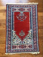 Full view of the prayer rug showing central red field with floral and geometric motifs and fringed ends.
