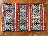 Top view of camel saddlebag textile showing red, black, white geometric kilim design with diamond shapes and cross patterns.