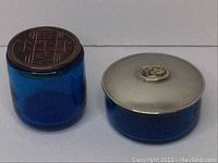 Photo showing both vintage blue cosmetic jars with their decorative lids on a white background.