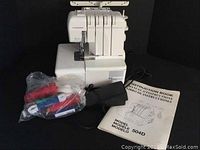 Front view showing serger machine, foot pedal, accessory bag and instruction manual