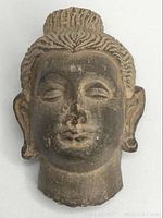 Full front view of stone Buddha head showing overall shape, patina, and size.