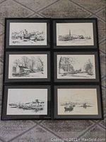 Six framed pen and ink prints laid out on floor showing detailed village, harbour, farmhouse, church, and castle scenes