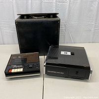 Photo of Kodak Carousel Custom 850H projector, Tiffen ShowCorder AV7200 tape player, and black carrying case on a table with a plain white backdrop.