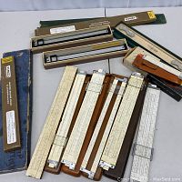 Overview of multiple slide rules, some in original boxes and cases, laid out showing their length and wear