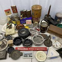 Overall lot view showing assorted ashtrays, tins, matchboxes and sign piece