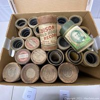 Box containing approximately two dozen cardboard tubes with Edison cylinder records, including a tall Gold Moulded container at center.