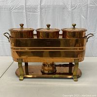 Front view of assembled copper chafing dish buffet set showing three lidded pots, copper stand and fuel burner