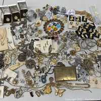 Wide view of assorted vintage costume jewelry including chains, brooches, pins, bracelets, and earrings with loose gemstones scattered throughout.