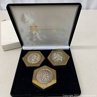 Three hexagonal brass paperweights displayed in black velvet-lined hinged box