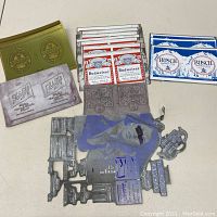 Overview of unrolled beer can labels and metal printing blocks for various beer brands arranged on flat surface.