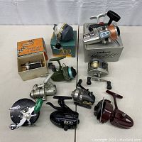 Photo showing 8 fishing reels on table including reels in original boxes; brands visible include Penn, Daiwa, Zebco